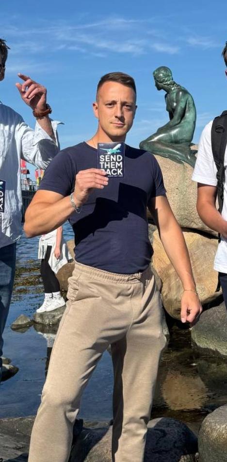 Man holds "Send Them Back" card by statue.