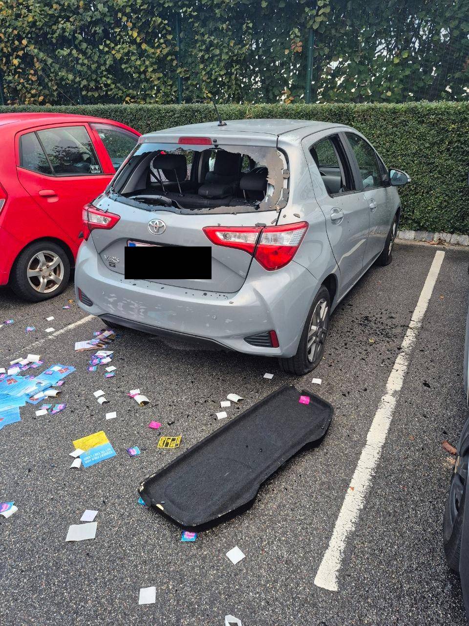 Car with smashed rear window and debris around.